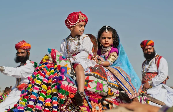 Boy and girl ride on a camel in the crowd of soldiers of Rajasthan