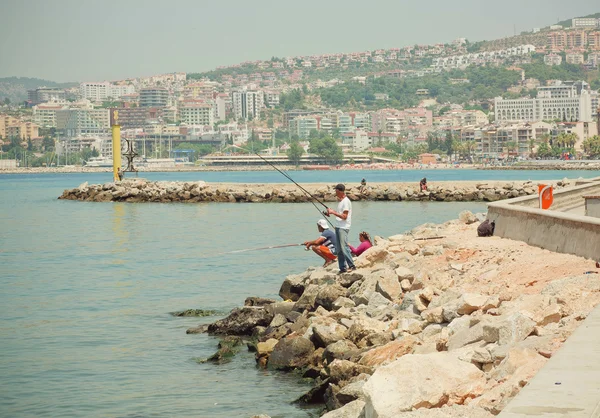 People fishing on a bay of Aegean sea at sunny day in modern city