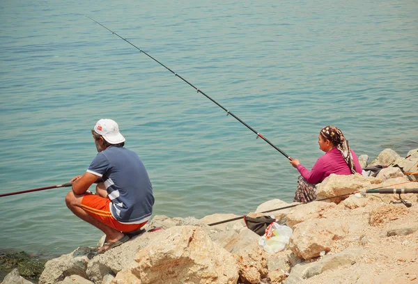 Woman with rod and man fishing on a bay with blue water of Aegean sea