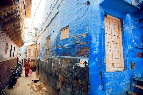 Narrow indian street with blue houses and rushing indian woman in India