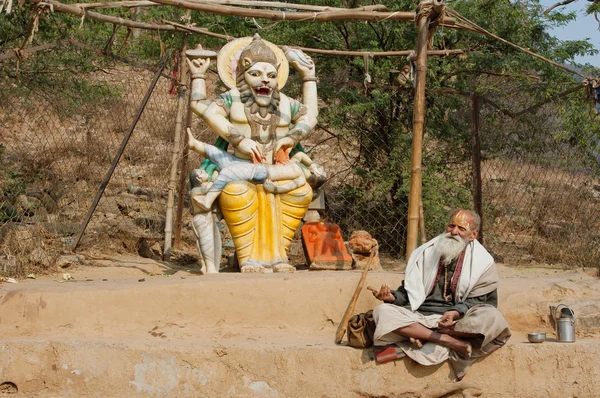 Poor man in clothes of Indian pilgrim resting by the sculpture of the hindu god Narasimha
