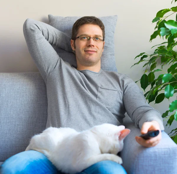 Man relaxing on the sofa with tv remote control. Watching TV with his cat.