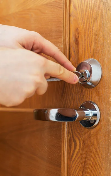Man's hand opening door with lock picker.