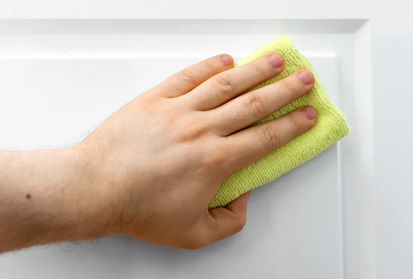 Man's hand wipes dust from white furniture.