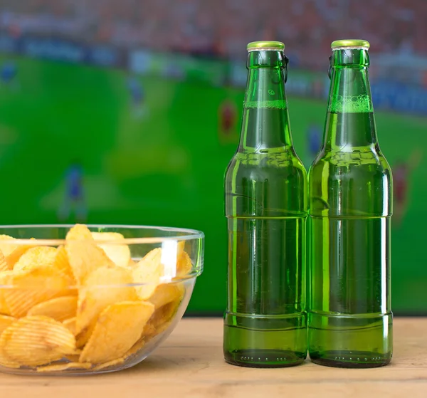 Beer and chips in front of TV with football match.