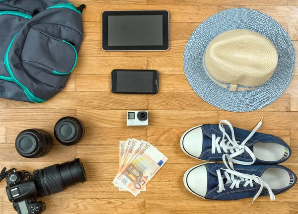 Travel accessories on the floor. Camera, phone, tablet, shoes, hat, money.