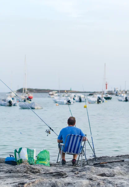 Man fishing in a bay near the boats.