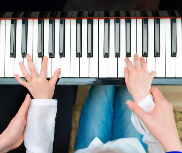 Woman teaching little girl to play the piano. Top view.