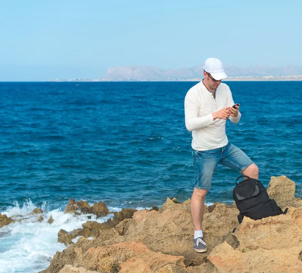 Male tourist with mobile phone standing near the sea.