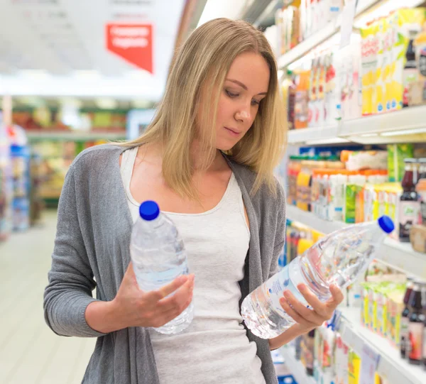 Woman choosing mineral water in grocery store.