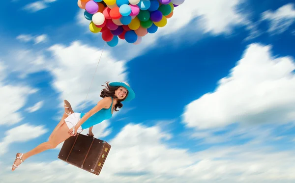 Woman holding balloons and flying above clouds