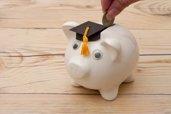 A white piggy bank with grad cap on weathered wood