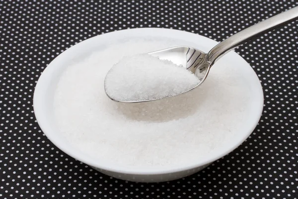 White bowl filled with sugar with a spoon on a black and white p
