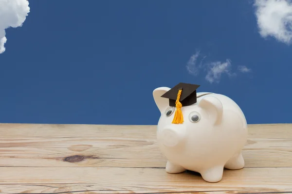 A white piggy bank with grad cap on weathered wood with sky back