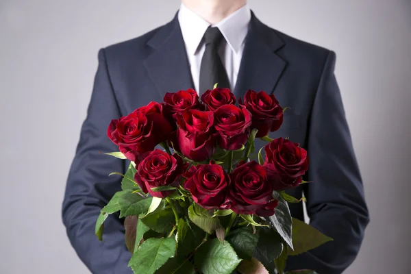 Man with bouquet of red roses on a gray background