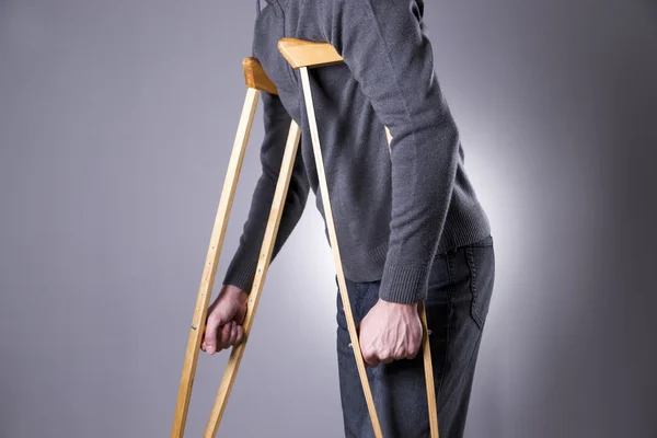 Man on crutches on a gray background