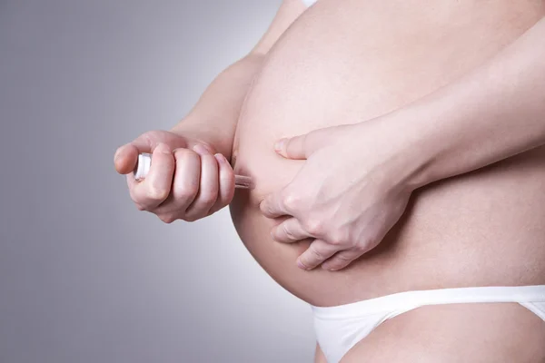 Young pregnant woman making injection in the stomach. Close-up studio shot