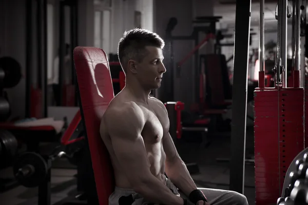 Handsome bodybuilder works out on athletic bench in gym. Perfect muscular male body