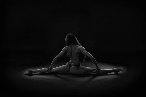 Beautiful muscular naked woman doing front split with right leg forward. Hanumanasana on a black background