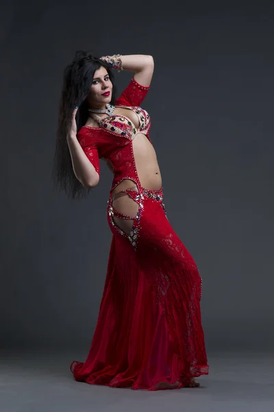 Young beautiful exotic eastern women performs belly dance in ethnic red dress on gray background