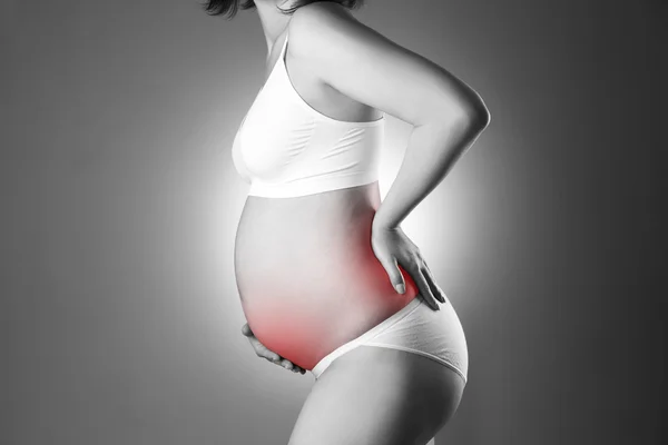 Caucasian pregnant woman in white lingerie with back and abdominal pain on gray studio background