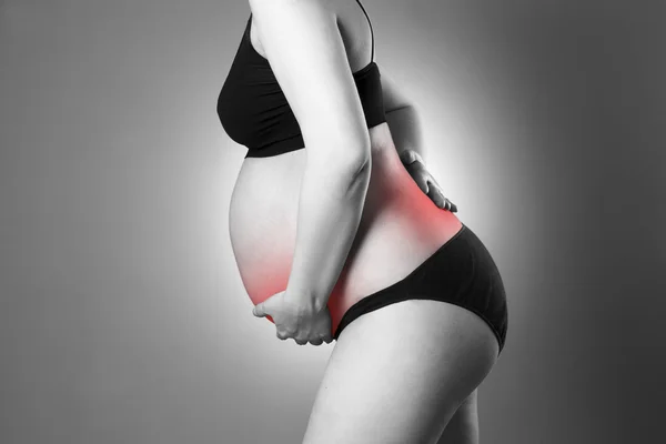 Caucasian pregnant woman in black lingerie with back and abdominal pain on gray studio background