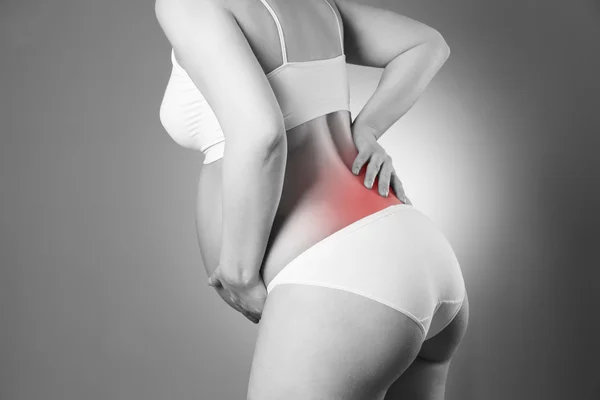 Caucasian pregnant woman in white lingerie with back pain on gray studio background