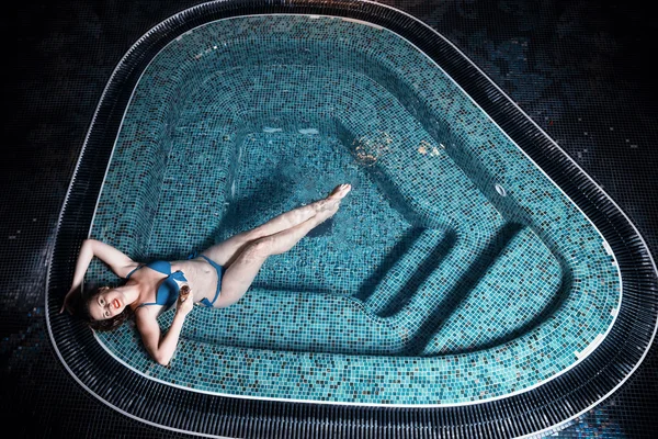 Beautiful young blonde caucasian woman in bikini relaxing in hot pool or jacuzzi at spa center