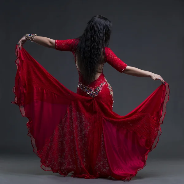 Young beautiful exotic eastern women performs belly dance in ethnic red dress with open back on gray background