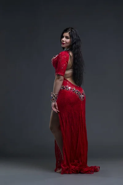 Young beautiful exotic eastern women performs belly dance in ethnic red dress on gray background