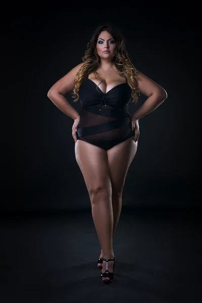 Young beautiful caucasian plus size model in swimsuit, xxl woman on black background