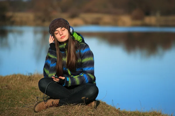 Young girl sitting on the ground and listening  music after hike