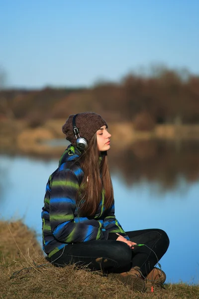 Young girl sitting on the ground and listening  music after hike