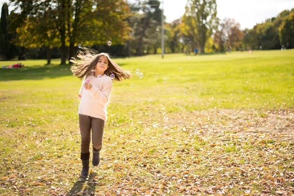 Adorable little girl outdoors at beautiful autumn day blows soap bubbles