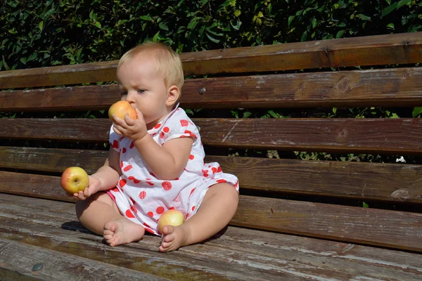 A small girl holds three apples