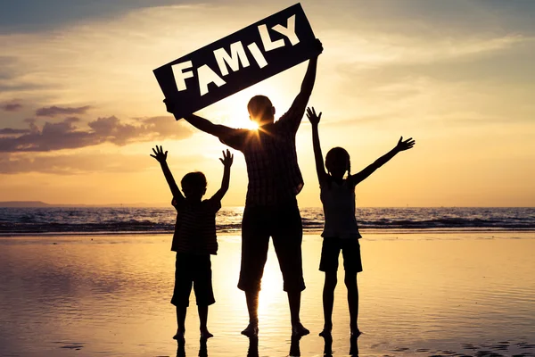 Happy family standing on the beach at the sunset time.