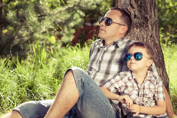 Father and son sitting near the tree in the garden.