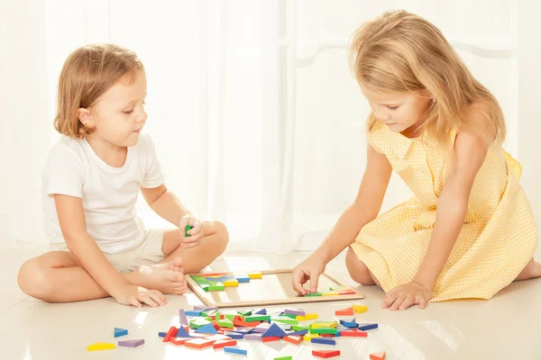 Two kids playing with wooden mosaic in their room on the floor