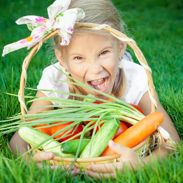 Happy little girl lying on the grass with a basket of vegetables