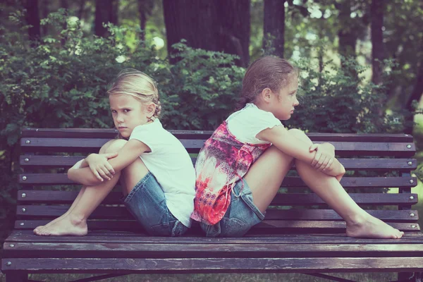 Two sad sister sitting on the bench in park