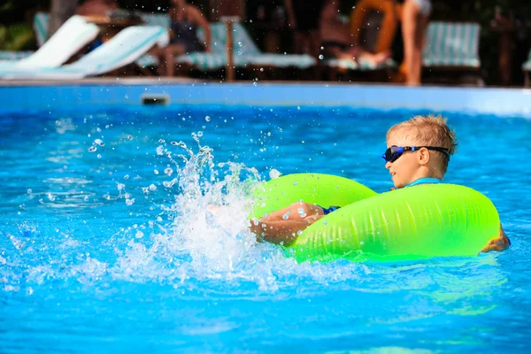 Little boy in life ring having fun at swimming pool