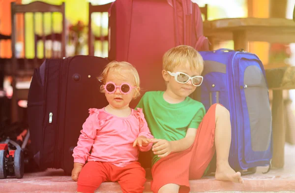 Little boy and toddler girl sitting on suitcases ready to travel