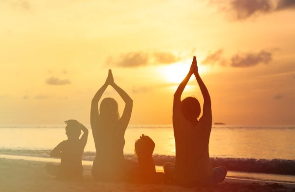 Family silhouettes doing yoga at sunset sea