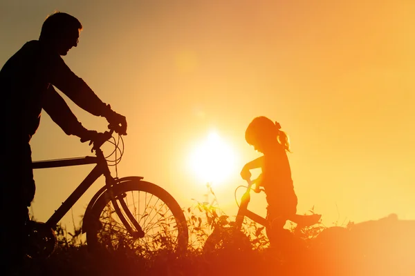 Father and daughter having fun riding bike at sunset, active family sport