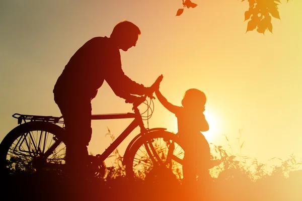 Father and daughter having fun riding bike at sunset, active family sport