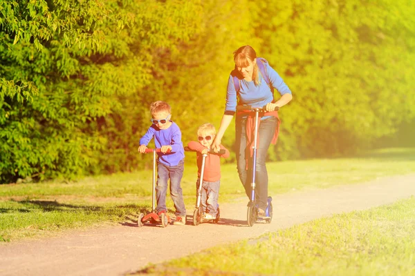 Mother with kids riding scooters in summer