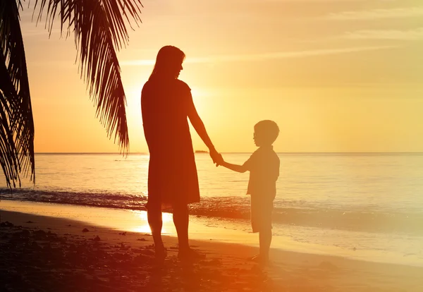 Silhouettes of mother and son holding hands at sunset