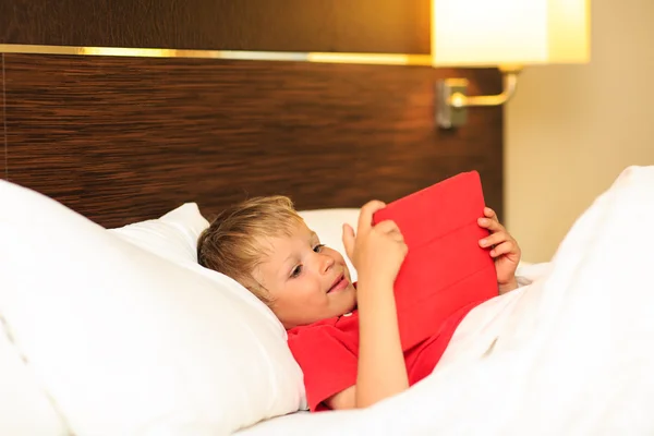 Little boy looking at touch pad lying in bed of hotel room
