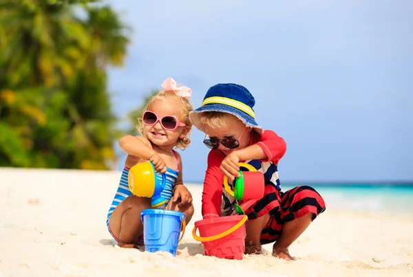 Cute little boy and toddler girl play with sand on beach