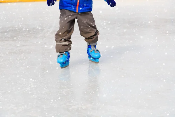 Child feet learning to skate on ice in winter